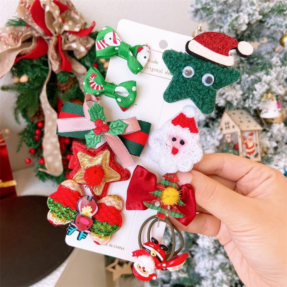 Hand holding a festive card of Christmas-themed hair clips including Santa, reindeer, tree, and star designs with ribbons and glitter.