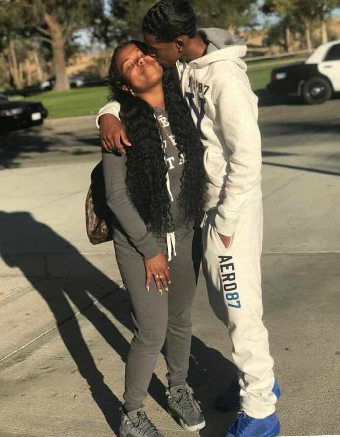 A young couple embracing affectionately outdoors; woman in gray sweatsuit with long curly hair, man in white Aeropostale hoodie and joggers.