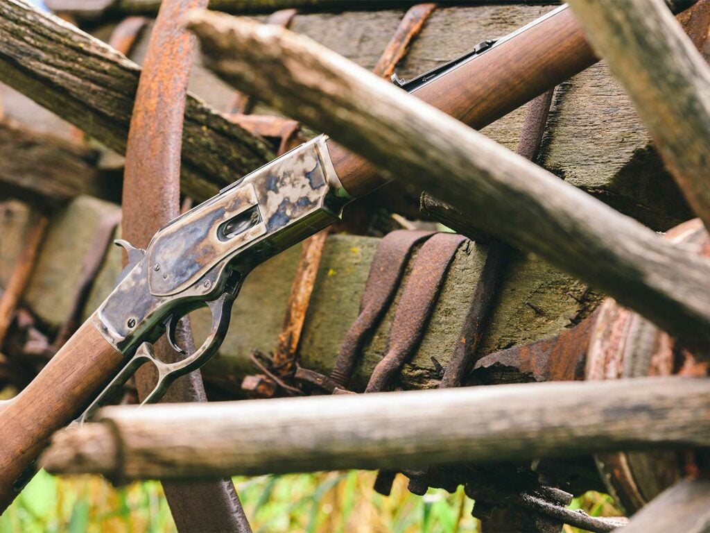 Vintage lever-action rifle with weathered metal and wood stock, nestled among rusted farm tools and wooden beams.