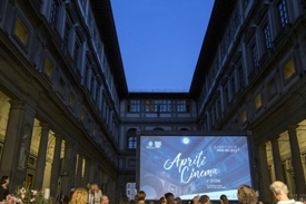 Outdoor cinema screening in a historic courtyard at dusk, with "Aprile Cinema" projected on a large screen and audience gathered below.
