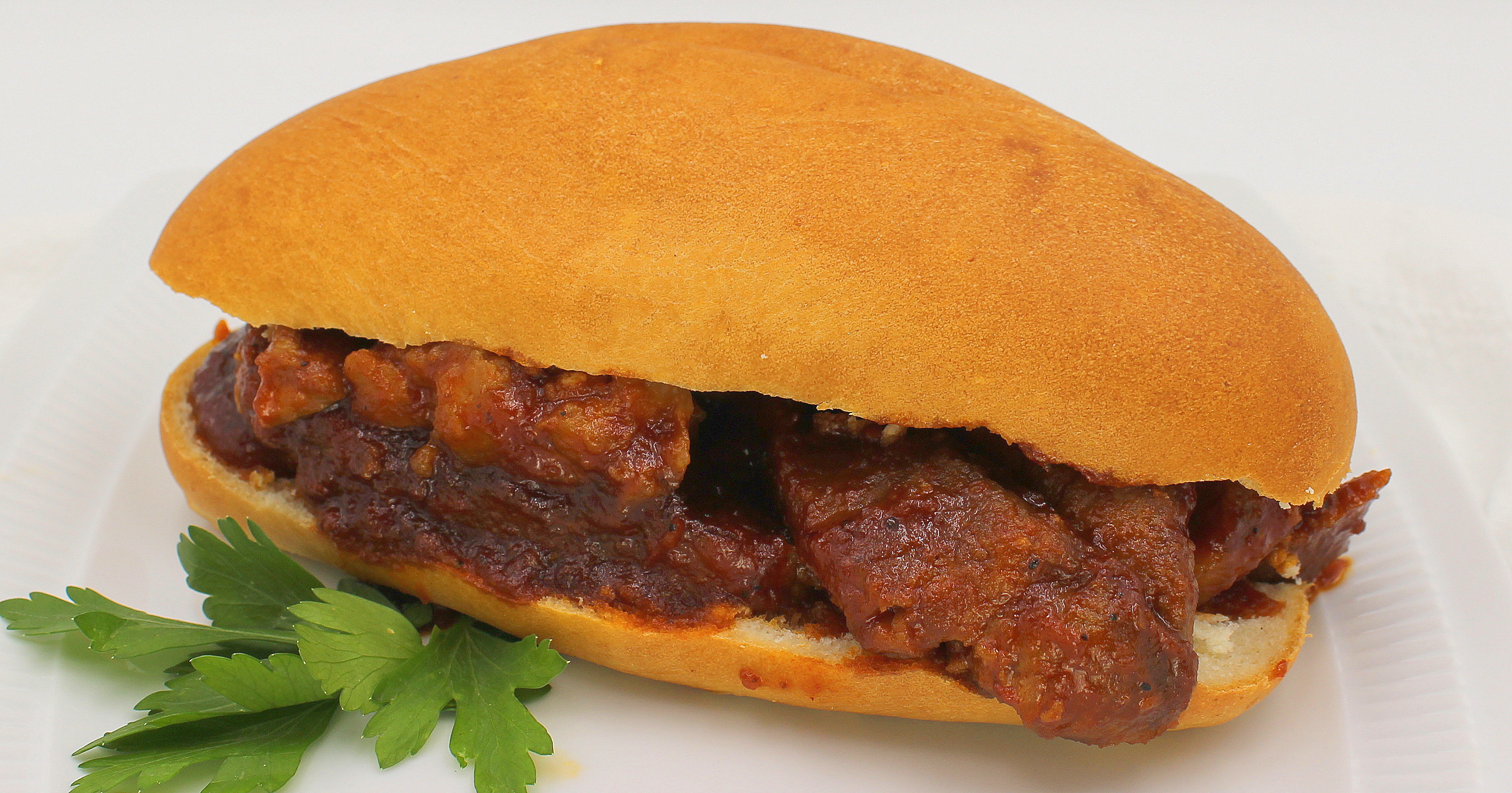 A hearty meatball sub sandwich with rich tomato sauce, served on a white plate with fresh parsley garnish.