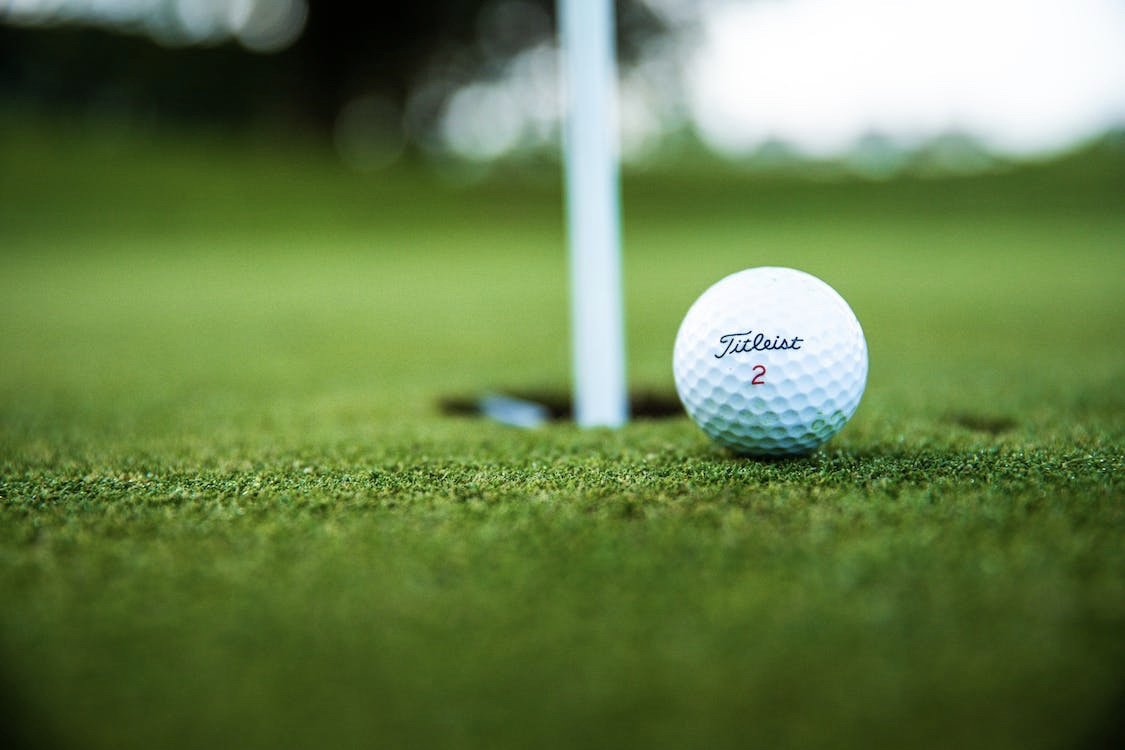 Titleist golf ball marked "2" resting on green grass near hole with flagstick in background.
