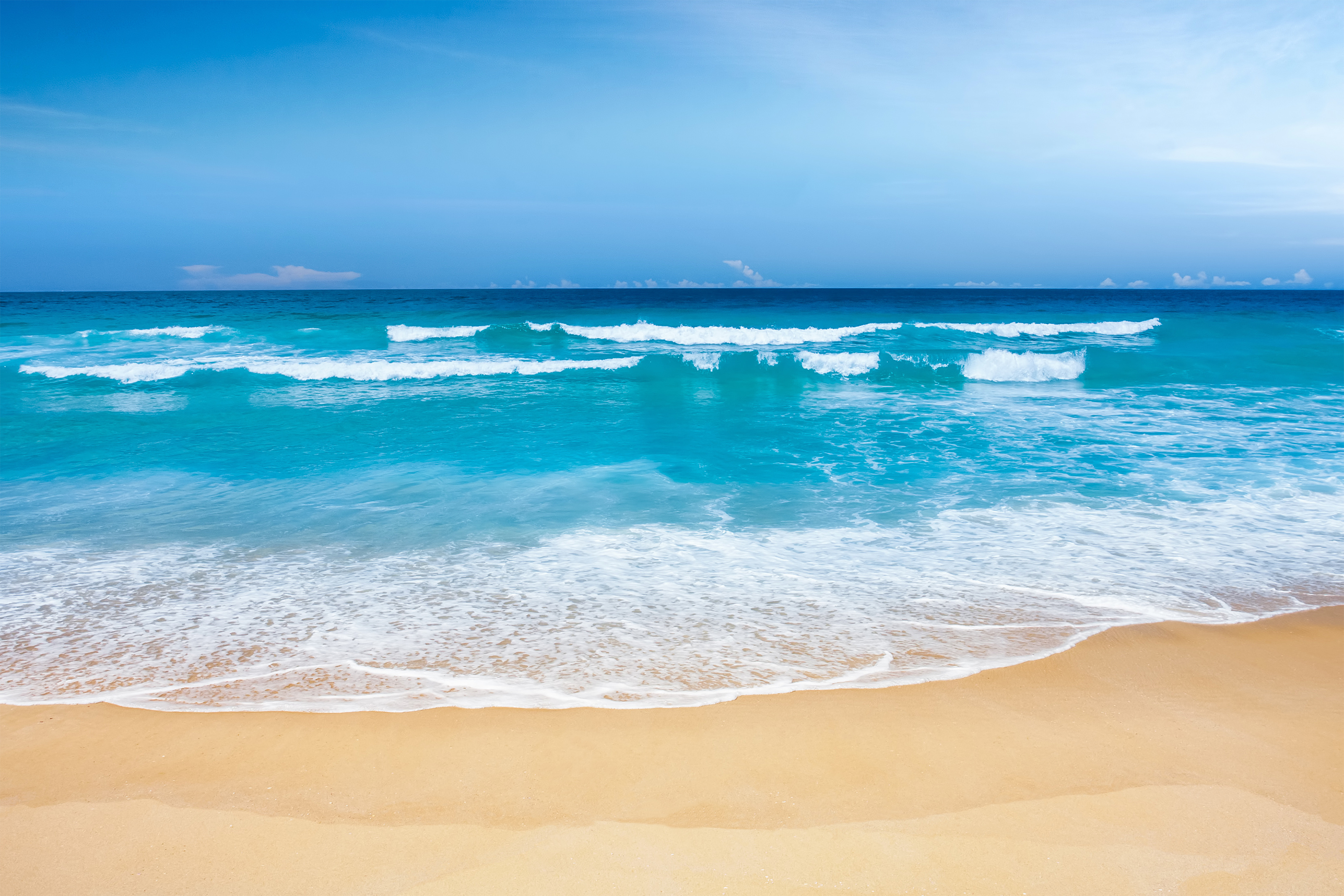 Turquoise ocean waves gently rolling onto a golden sandy beach under a clear blue sky.