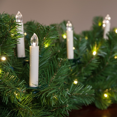 White LED candle-style lights nestled in green artificial pine garland, softly glowing with warm white illumination.