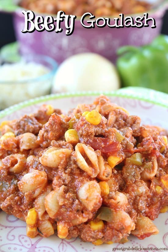 A hearty serving of beefy goulash with shell pasta, corn, tomatoes, and green peppers on a decorative plate.