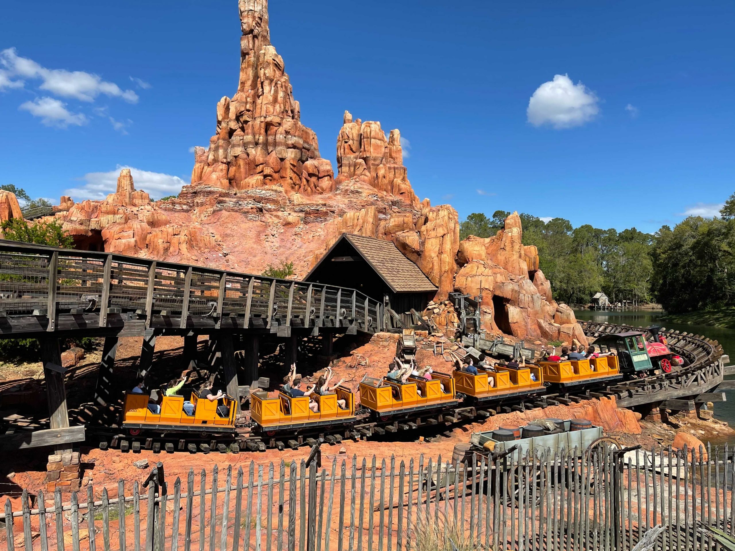 Guests ride the Big Thunder Mountain Railroad roller coaster through a rugged desert canyon landscape under a bright blue sky.