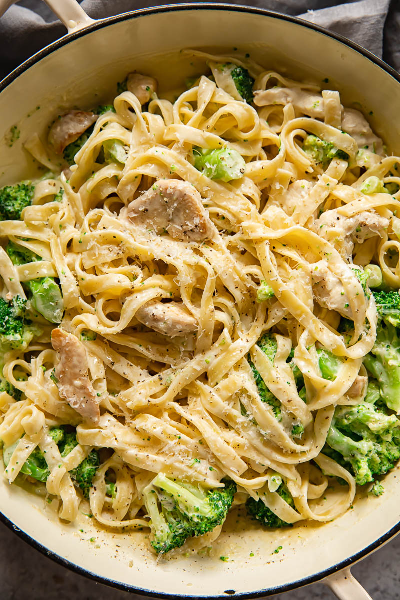 Creamy chicken and broccoli fettuccine in a white enamel pan, garnished with grated Parmesan and black pepper.