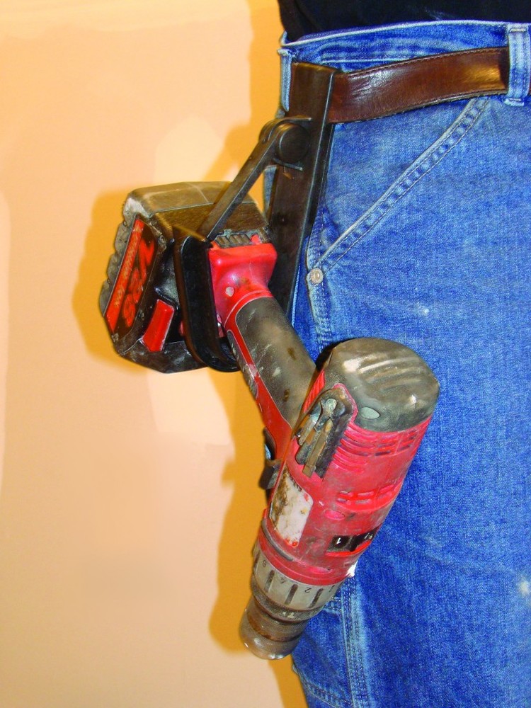 Red cordless drill secured in a black belt holster on a worker’s hip, showing wear and use.