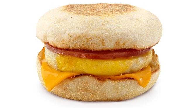 Classic breakfast sandwich with egg, cheese, tomato, and English muffin on white background.