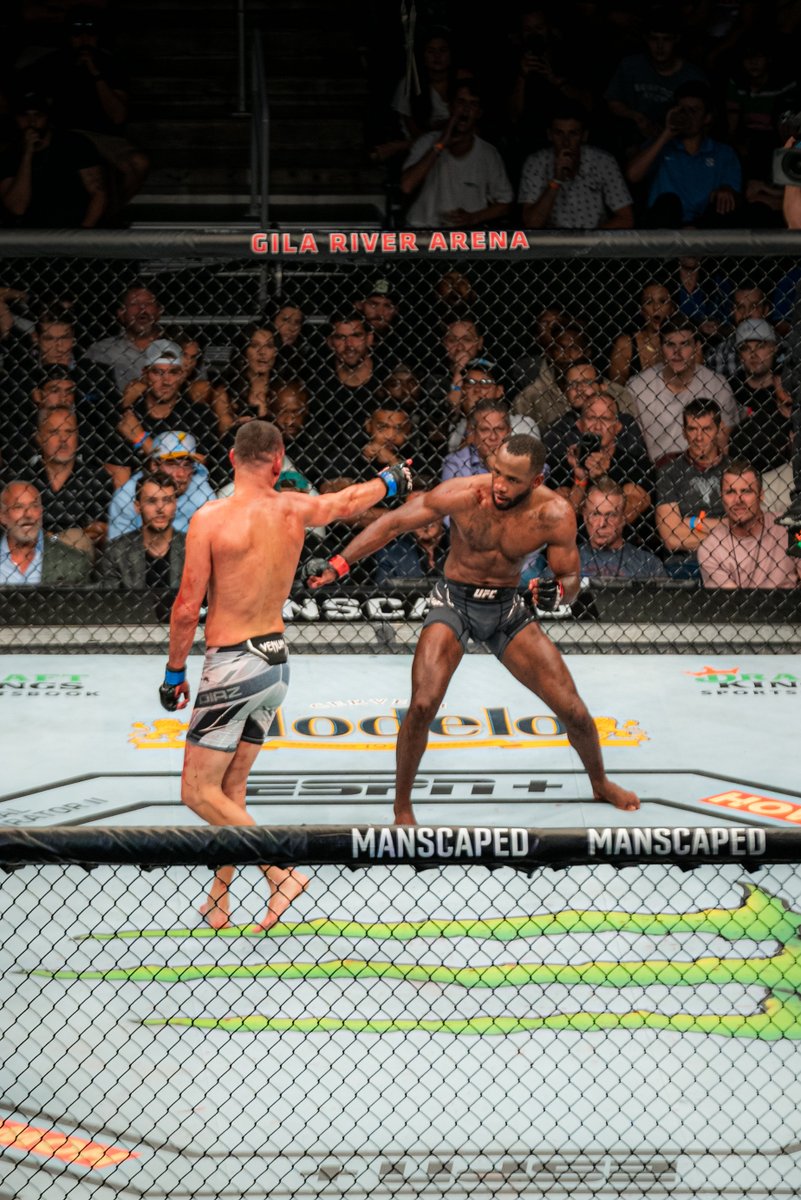 Two UFC fighters exchange strikes inside the octagon at Gila River Arena with crowd watching.