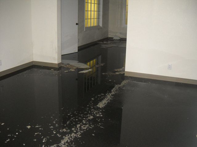 Flooded interior room with black epoxy floor, peeling debris, and yellow-lit barred windows.