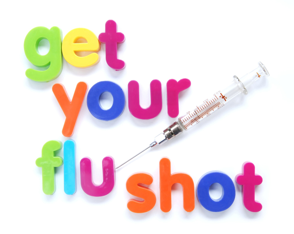 Colorful magnetic letters spell "get your flu shot" beside a medical syringe on white background.