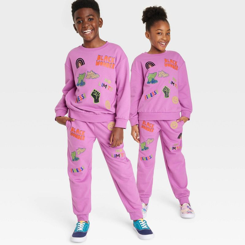 Two smiling Black children wearing matching purple "Black Wonder No Limits" graphic sweatshirt and jogger sets.