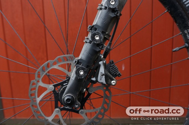 Close-up of a mountain bike’s front disc brake and suspension fork against a red wooden background.
