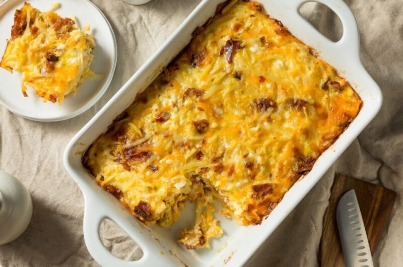 Cheesy hash brown casserole with bacon in a white baking dish, one serving plated beside it.