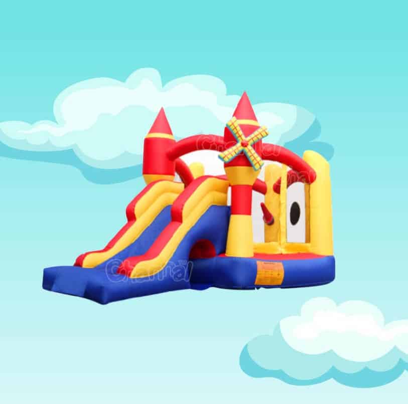 Colorful inflatable bouncer with castle towers, dual slides, and windmill decoration against a sky background.