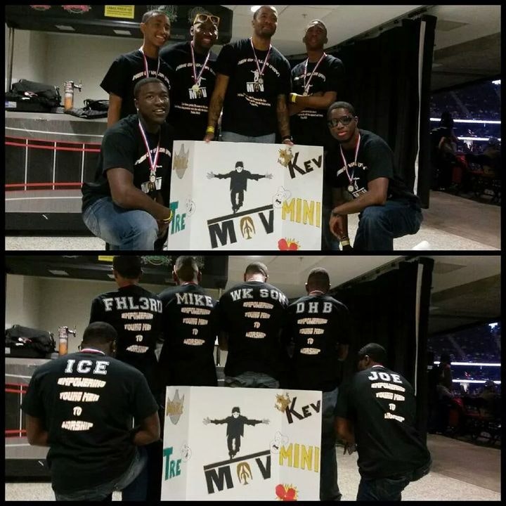 Group of young men in matching black t-shirts with medals, posing with a handmade "MOV Mini" poster at an event.