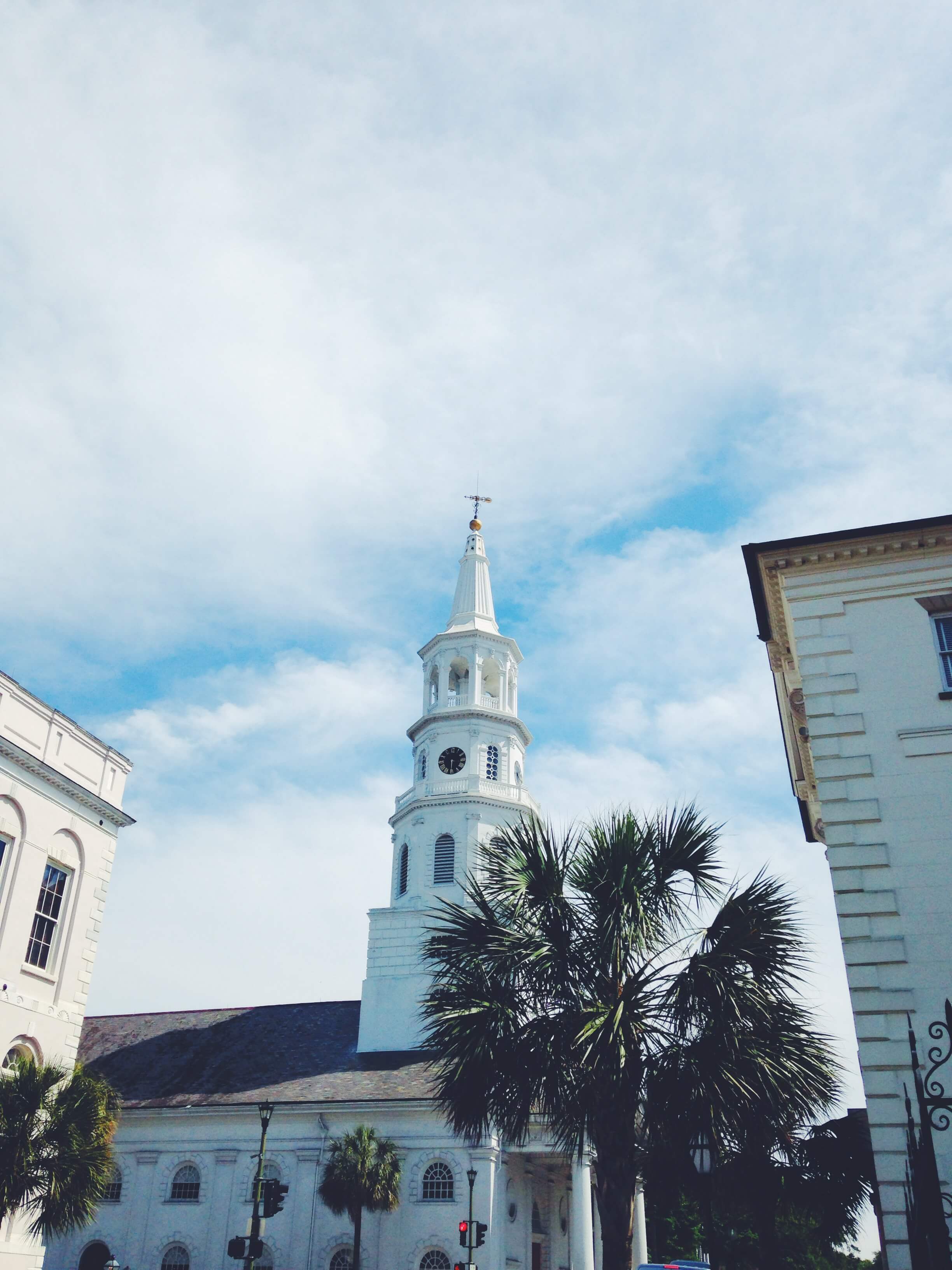 White steepled church with palm trees and historic architecture under a partly cloudy sky.