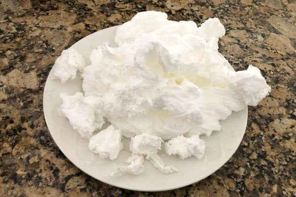 A white plate piled with fluffy, freshly whipped egg whites on a granite countertop.