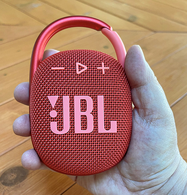 Red JBL Clip 4 portable Bluetooth speaker with carabiner, held in hand on wooden background.