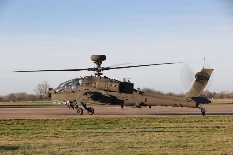 AH-64 Apache attack helicopter on a runway with rotors spinning, ready for takeoff.