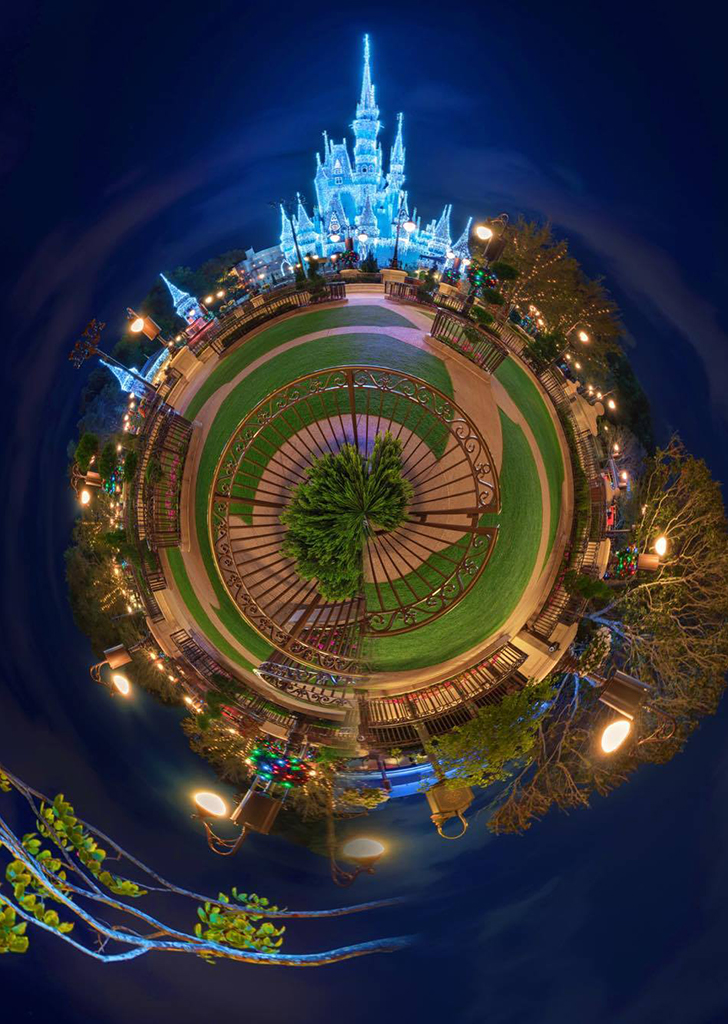 A 360-degree "tiny planet" night view of Cinderella Castle illuminated in blue, surrounded by circular pathways, lampposts, and festive greenery.