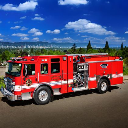Red fire engine parked on asphalt with city skyline and green hills in background under blue sky.