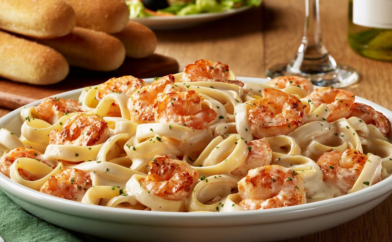 Creamy fettuccine Alfredo with grilled shrimp, garnished with parsley, served in a white bowl beside breadsticks and wine.