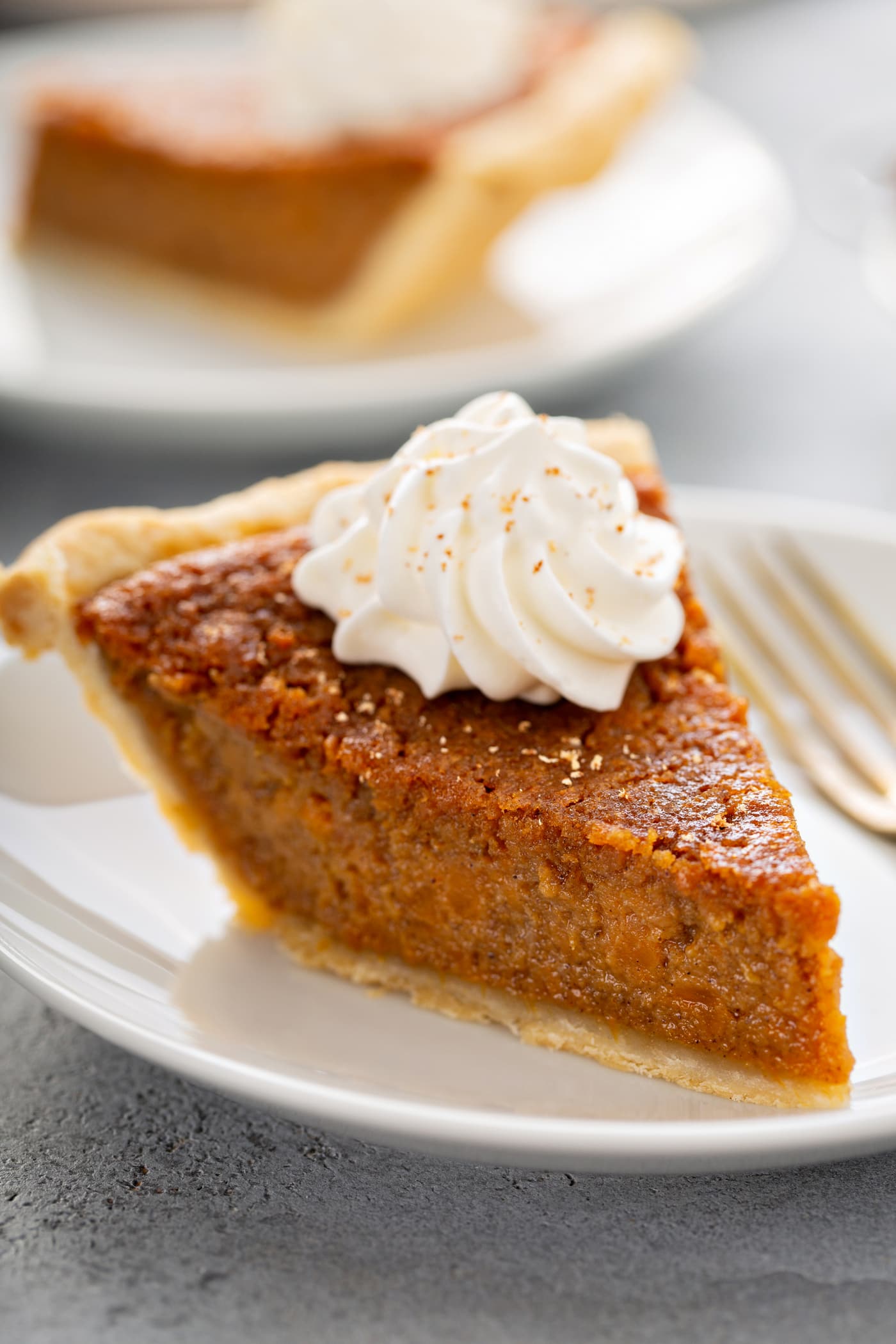 A slice of golden-brown sweet potato pie topped with whipped cream and a sprinkle of cinnamon on a white plate.