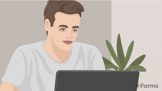 Young man smiling while working on a laptop beside a green plant in a modern home office setting.