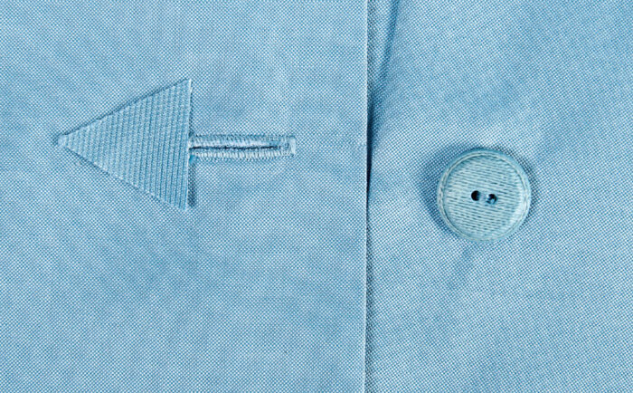 Close-up of a light blue shirt featuring an embroidered arrow detail and matching button.