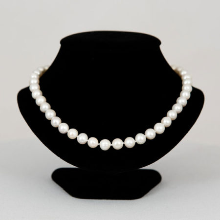 Elegant white pearl necklace displayed on a black velvet bust stand against a neutral background.