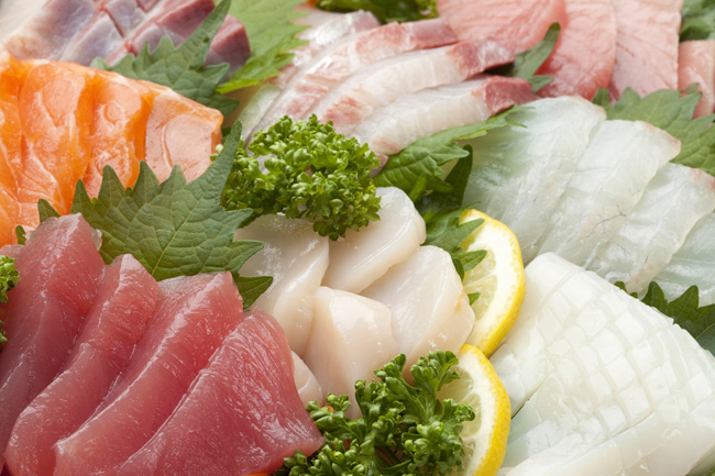 Fresh sashimi platter featuring salmon, tuna, scallops, squid, and white fish garnished with shiso leaves and lemon.