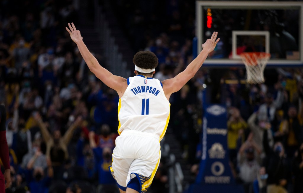 Klay Thompson celebrating with arms raised after a shot, wearing Golden State Warriors #11 jersey in a packed arena.