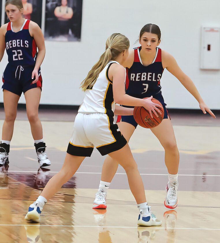 High school girls basketball game: defender in white guards Rebel #3 with ball, teammate #22 watches nearby.
