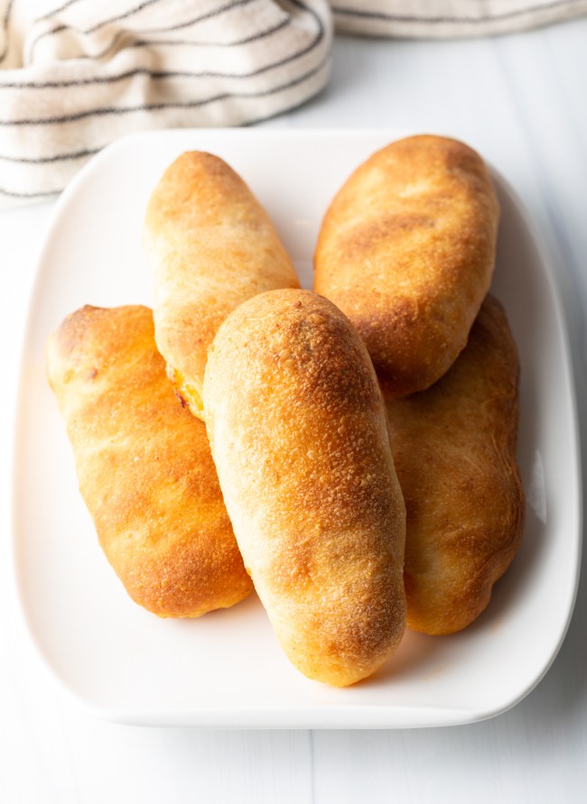 Golden-brown baked calzones on a white plate with striped cloth background.