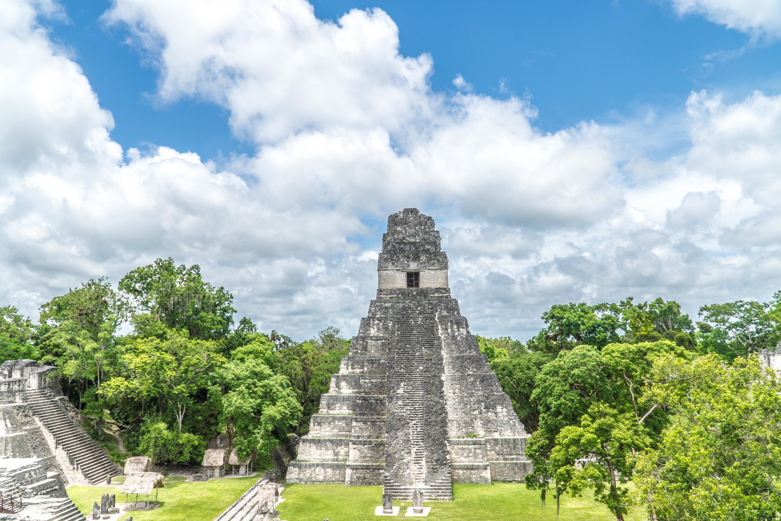 Ancient Mayan pyramid temple rising from lush jungle under a partly cloudy sky at Tikal, Guatemala.