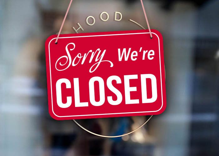 Red "Sorry We're Closed" sign hanging on a glass door with blurred interior background.