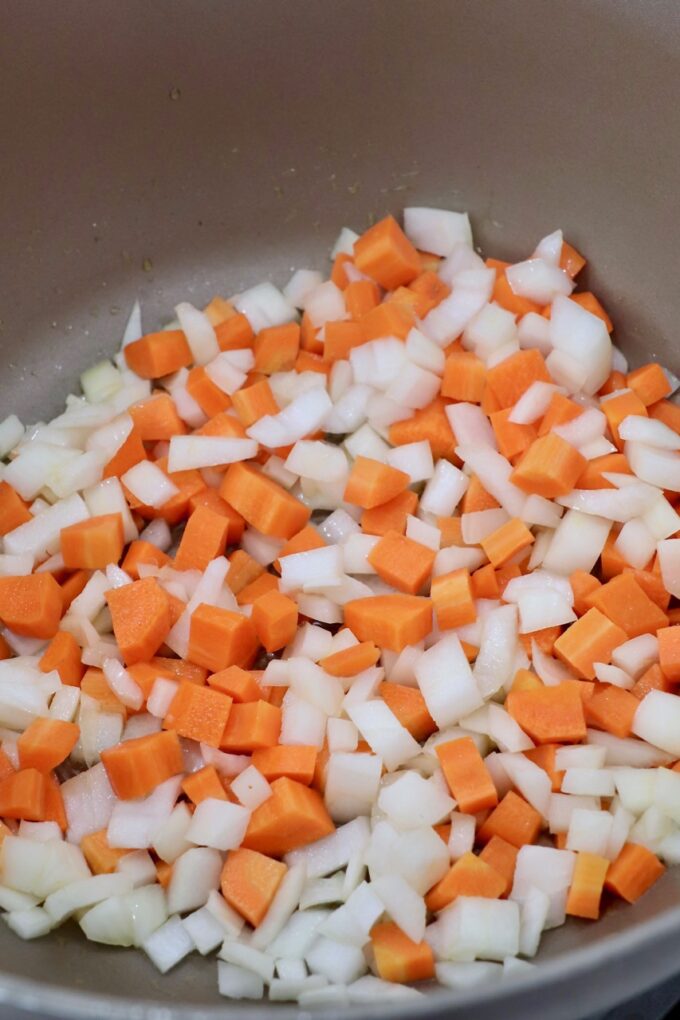Diced onions and carrots sautéing in a pan, ready for a savory dish.