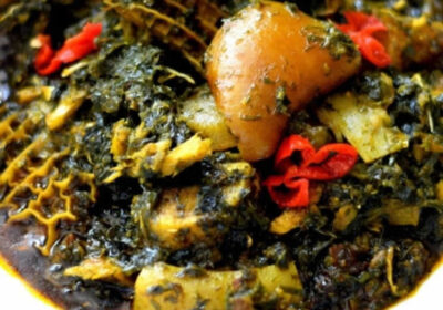 A rich, dark Nigerian spinach stew with meat, offal, and red peppers, served in a white bowl.