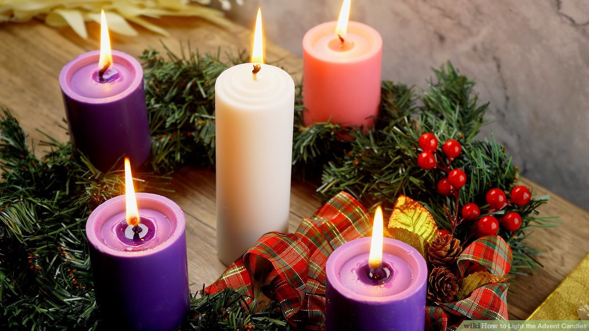 Five lit Advent candles-three purple, one pink, one white-arranged in a wreath with evergreen, berries, and plaid ribbon.