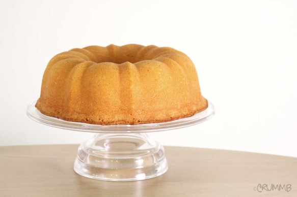 Golden-brown bundt cake on a clear glass cake stand against a white background.