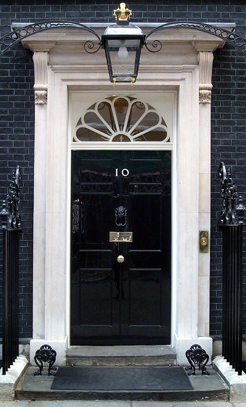 Iconic black door of 10 Downing Street, London, with gold number 10, fanlight window, and ornate lantern above.