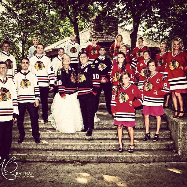A wedding party posing on stone steps, all wearing Chicago Blackhawks jerseys-bride in white gown at center.