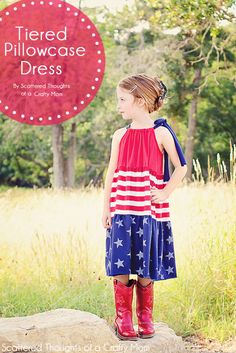 Girl wearing a red, white, and blue tiered pillowcase dress with star pattern, standing outdoors in a field.