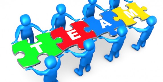 Blue figures assembling colorful puzzle pieces spelling "TEAM" to symbolize collaboration and unity.