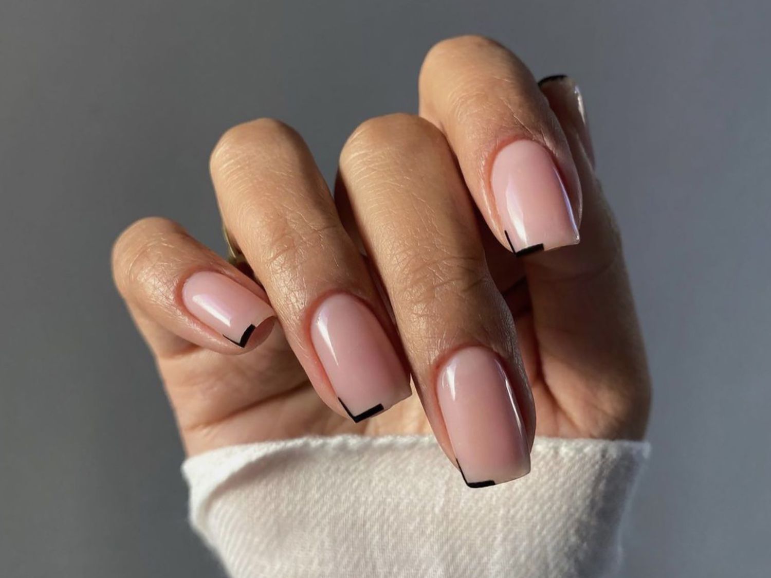 Hand with elegant nude manicure and minimalist black geometric tip accents on almond-shaped nails.