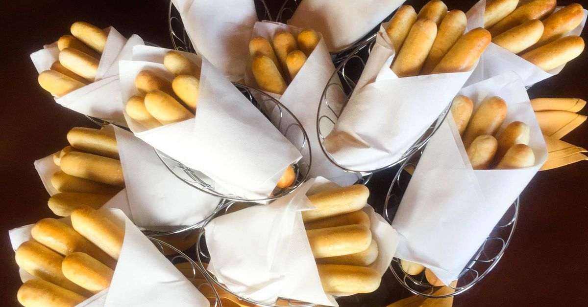 Freshly baked breadsticks served in wire baskets lined with white paper napkins, arranged on a dark wooden table.