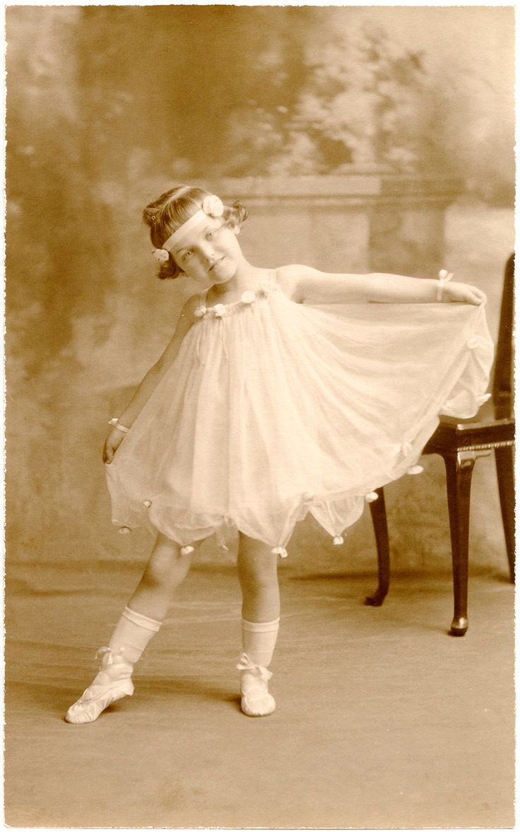 Vintage sepia portrait of a young girl in a ballet pose, wearing a sheer white dress and pointe shoes, with floral hair accessories.