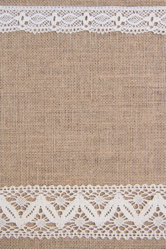 Rustic burlap fabric with white lace trim at top and bottom edges, textured natural background.